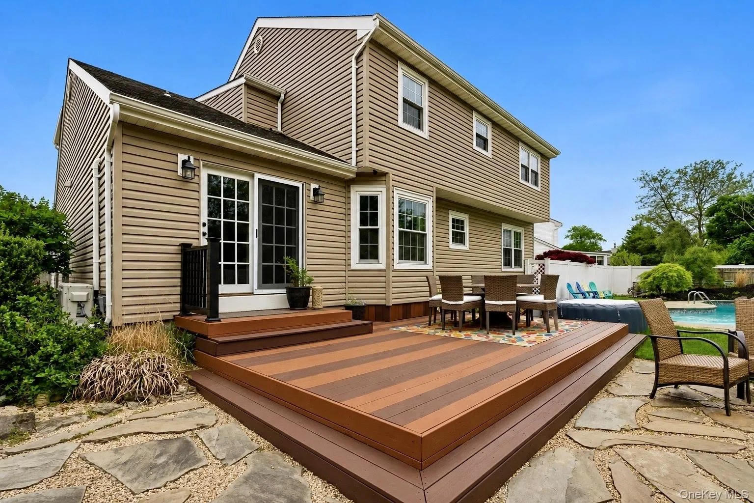 Multi-level composite deck with striped wood-finish boards, sliding glass doors, and a stone paver patio Multi-level composite deck with striped wood-finish boards, sliding glass doors, and a stone paver patio