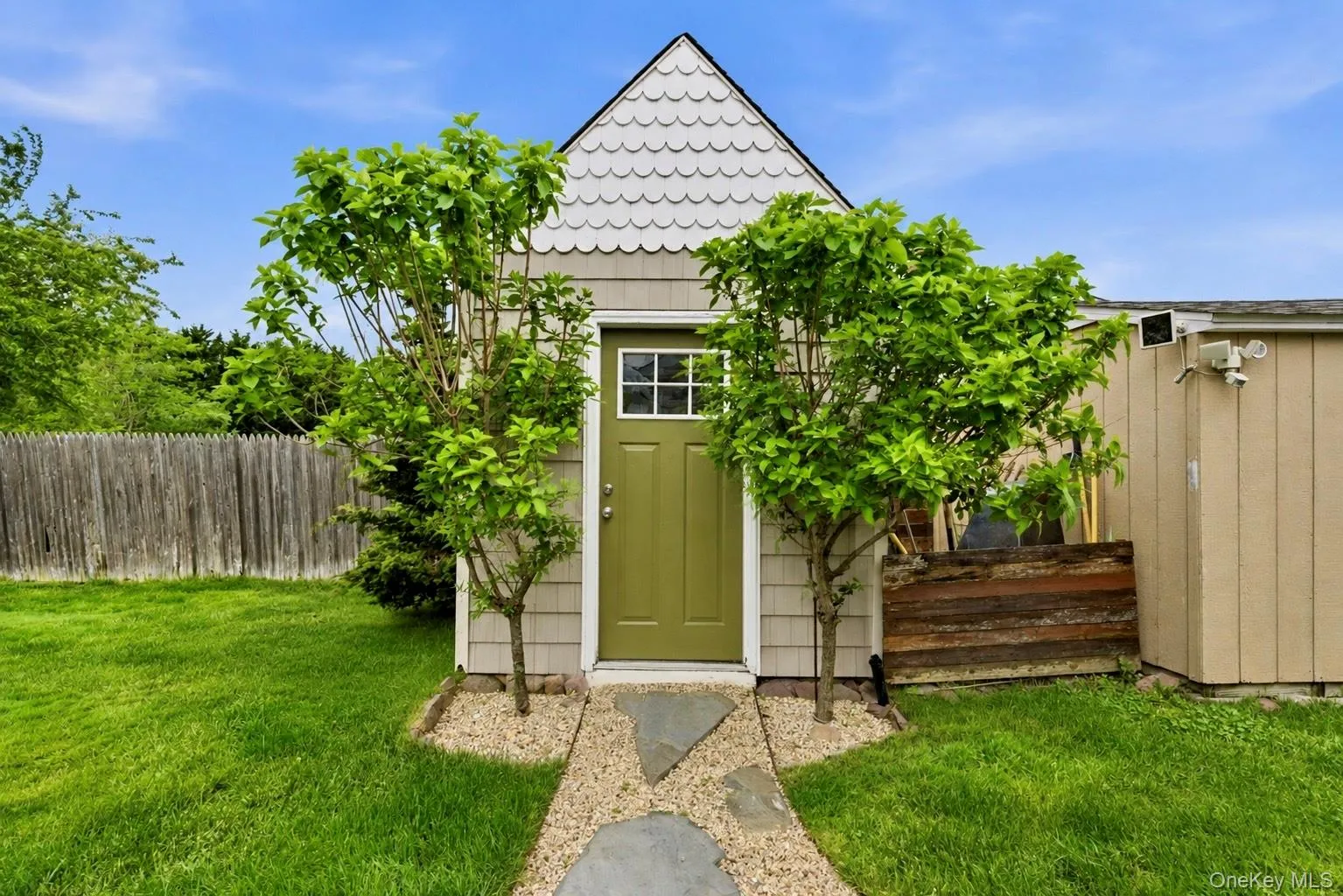Detached accessory structure featuring scallop shingle siding, a pitched roofline, and a green entry door with a divided light window Detached accessory structure featuring scallop shingle siding, a pitched roofline, and a green entry door with a divided light window