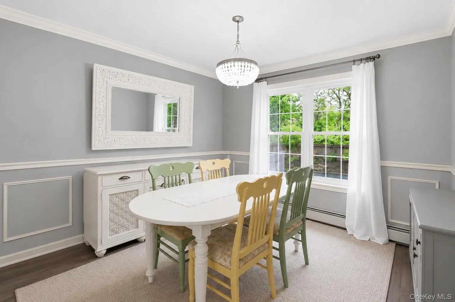 Dining area featuring a crystal chandelier, crown molding, chair rail with wall paneling, wood-finish flooring, and a large window with white trim Dining area featuring a crystal chandelier, crown molding, chair rail with wall paneling, wood-finish flooring, and a large window with white trim