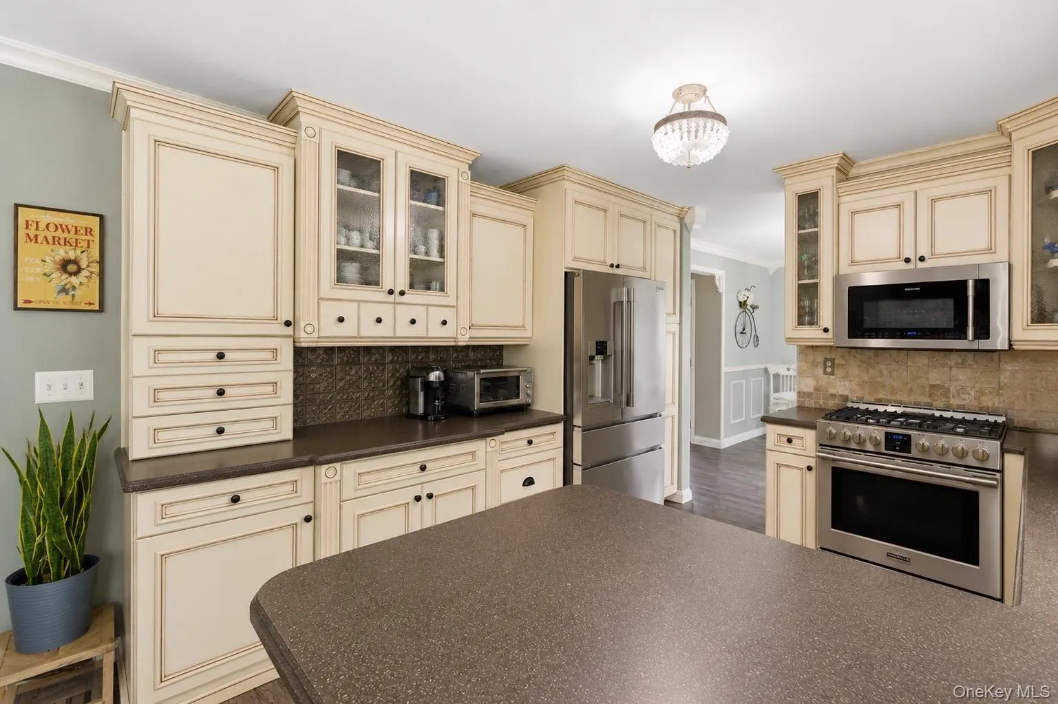 Kitchen featuring light-toned cabinetry with dark hardware, a brown speckled countertop, stainless steel appliances, and a decorative tile backsplash Kitchen featuring light-toned cabinetry with dark hardware, a brown speckled countertop, stainless steel appliances, and a decorative tile backsplash