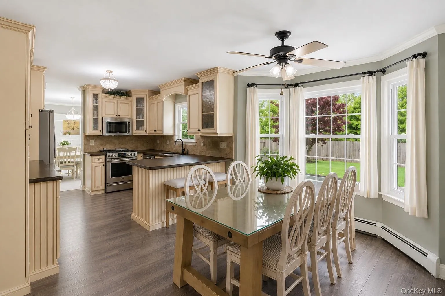 Kitchen and dining area featuring wood-finish flooring, cream cabinetry, a stone-tile backsplash, and a breakfast bar with beadboard paneling Kitchen and dining area featuring wood-finish flooring, cream cabinetry, a stone-tile backsplash, and a breakfast bar with beadboard paneling