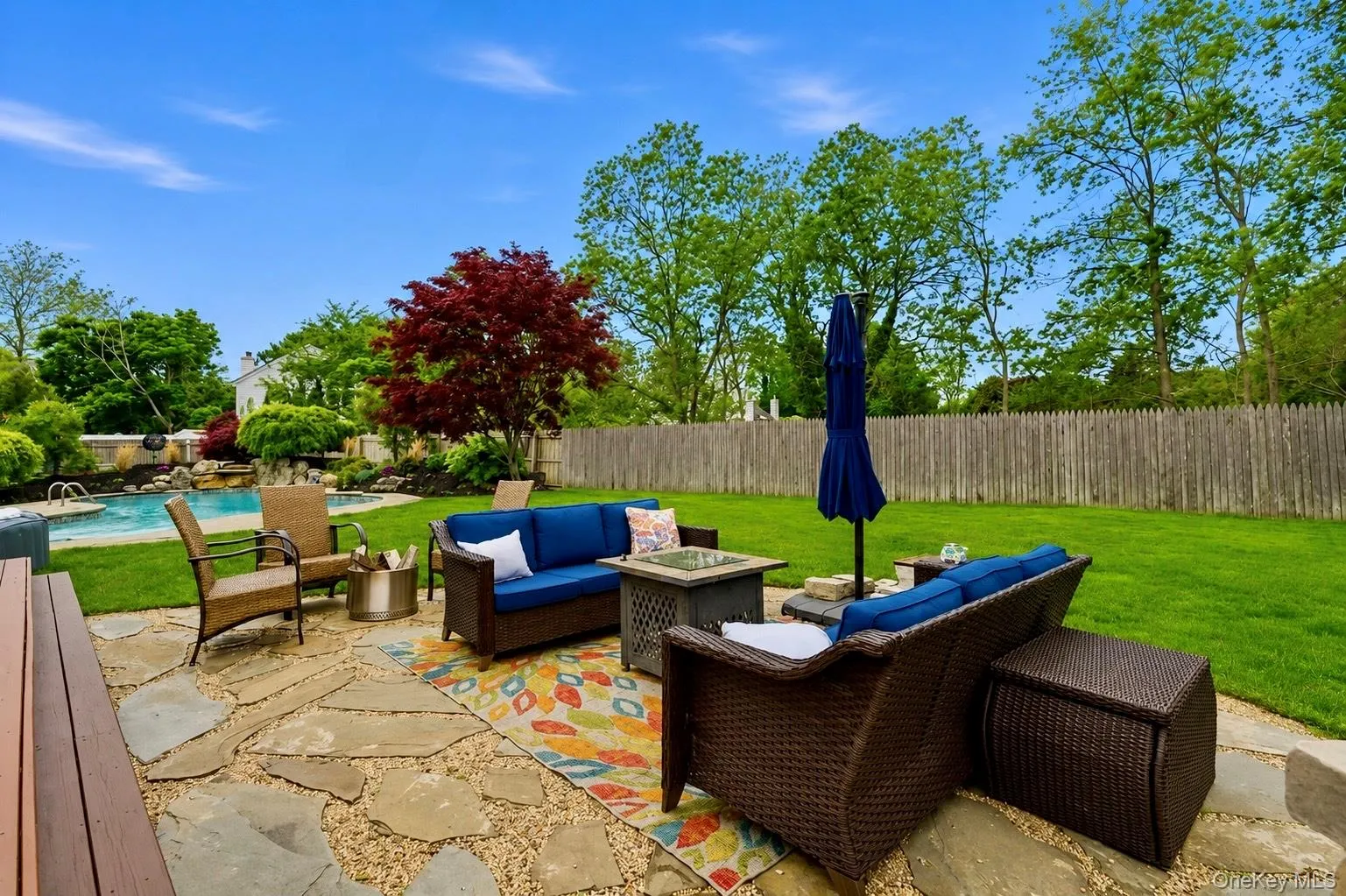 Expansive backyard featuring a natural stone patio, manicured lawn, inground swimming pool with waterfall feature, a red Japanese maple tree, and a wooden privacy fence Expansive backyard featuring a natural stone patio, manicured lawn, inground swimming pool with waterfall feature, a red Japanese maple tree, and a wooden privacy fence