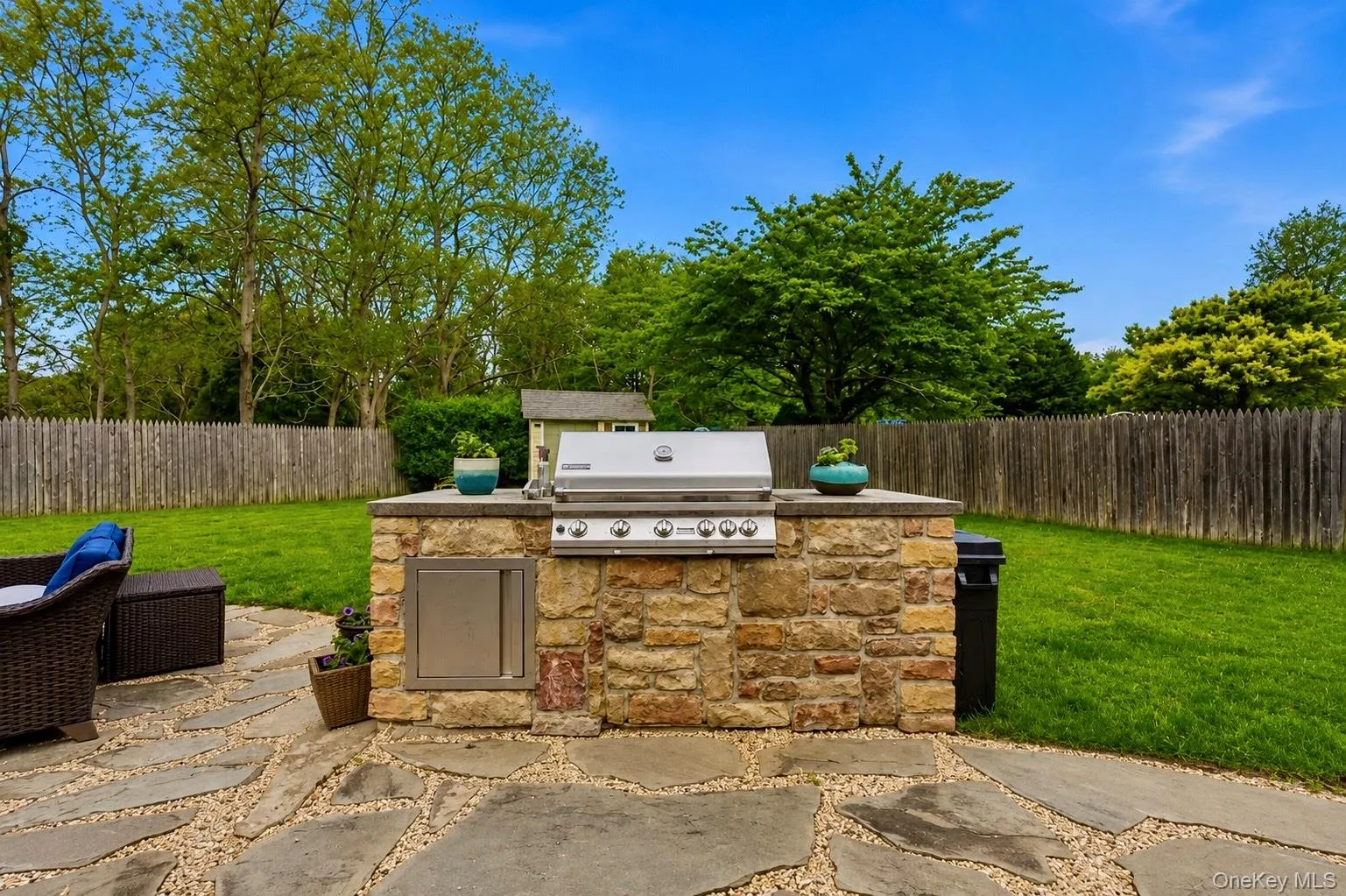 Outdoor kitchen with a built-in stainless steel grill set in a stacked stone base with a neutral countertop Outdoor kitchen with a built-in stainless steel grill set in a stacked stone base with a neutral countertop