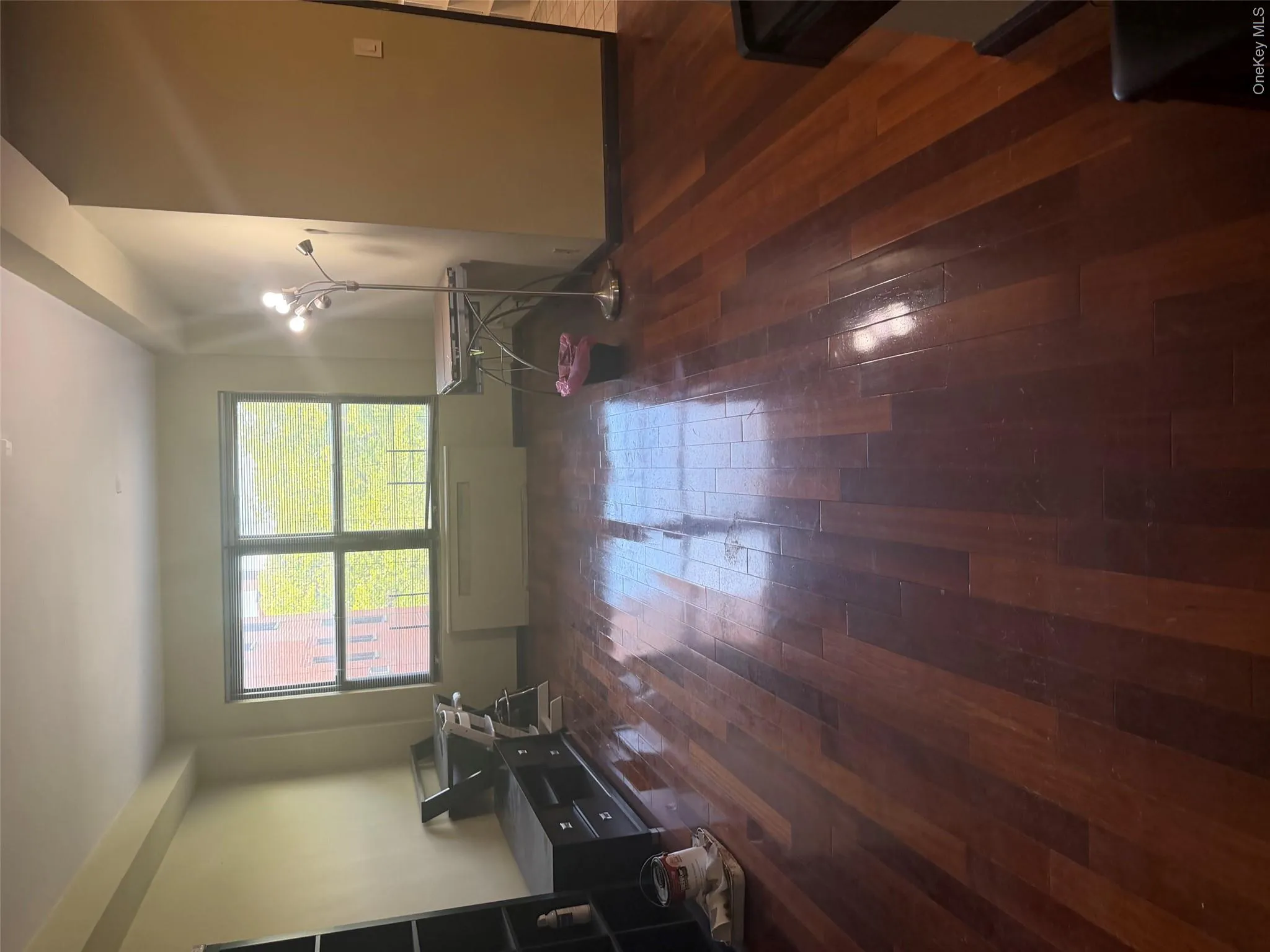 Spacious room featuring rich wood-finish flooring, a large window, light-toned walls, and a built-in wall unit Spacious room featuring rich wood-finish flooring, a large window, light-toned walls, and a built-in wall unit