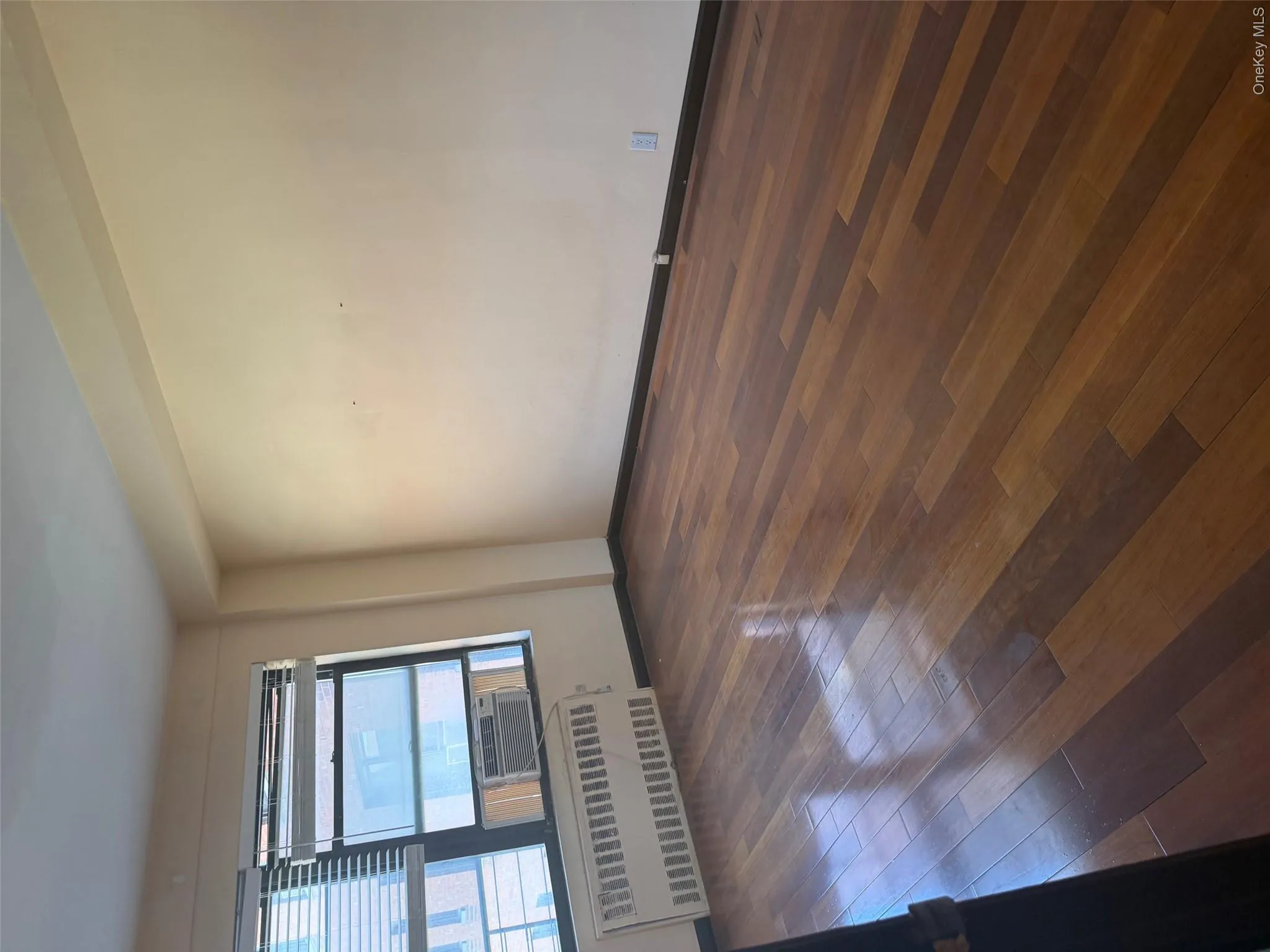 Room featuring wood-finish flooring, light-toned walls, and a window with horizontal blinds Room featuring wood-finish flooring, light-toned walls, and a window with horizontal blinds