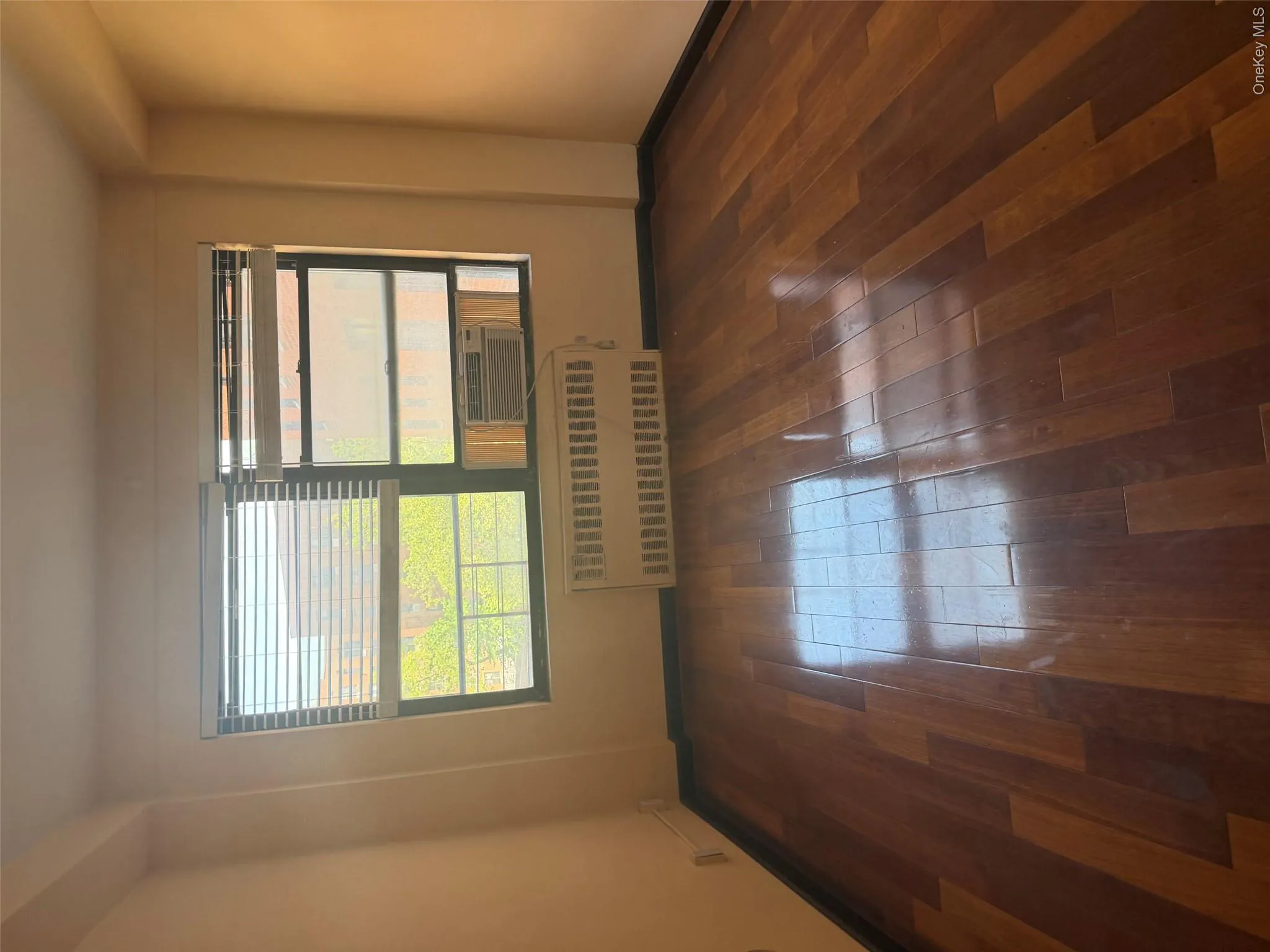 Hardwood flooring throughout, featuring a multi-pane window with horizontal blinds, an air conditioning unit, and a radiator Hardwood flooring throughout, featuring a multi-pane window with horizontal blinds, an air conditioning unit, and a radiator