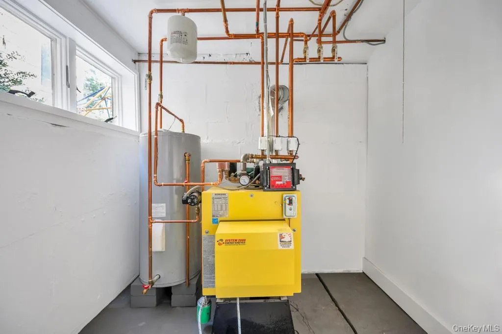 Basement utility room featuring a yellow boiler system, water heater, and extensive copper piping Basement utility room featuring a yellow boiler system, water heater, and extensive copper piping