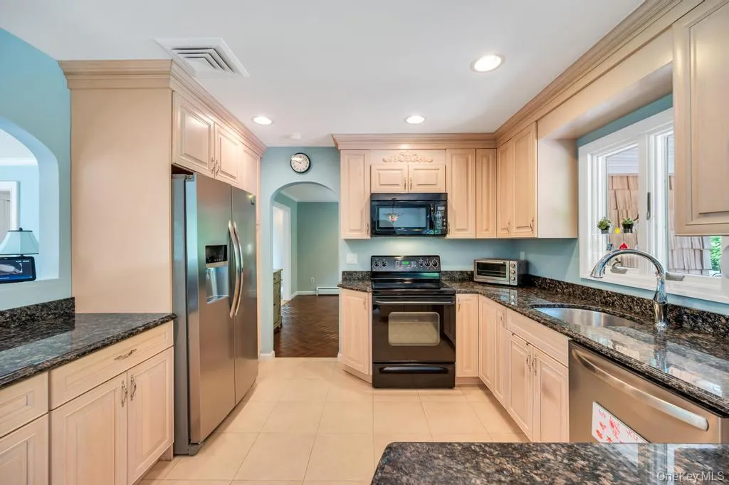 Kitchen featuring light-tone wood cabinetry with crown molding, dark speckled countertops, and a stainless steel refrigerator Kitchen featuring light-tone wood cabinetry with crown molding, dark speckled countertops, and a stainless steel refrigerator