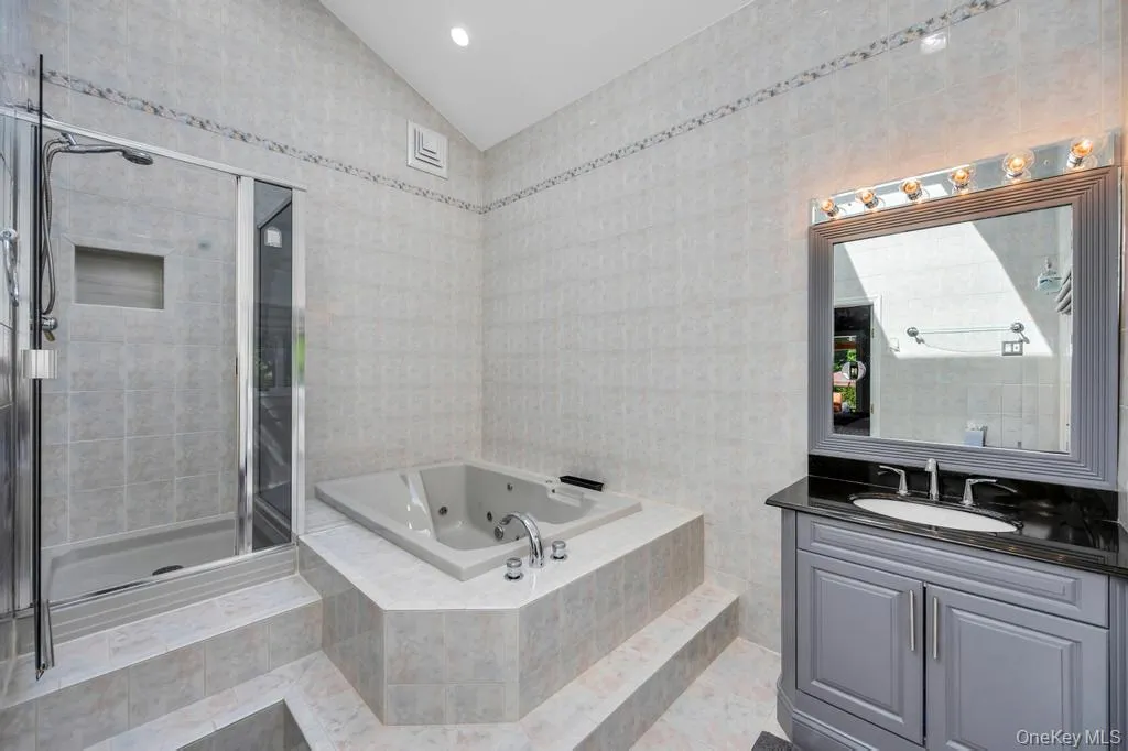 Bathroom featuring a shower enclosure with a built-in niche, a built-in tub, a vanity with a dark countertop and undermount sink, a framed mirror, and integrated vanity lighting Bathroom featuring a shower enclosure with a built-in niche, a built-in tub, a vanity with a dark countertop and undermount sink, a framed mirror, and integrated vanity lighting