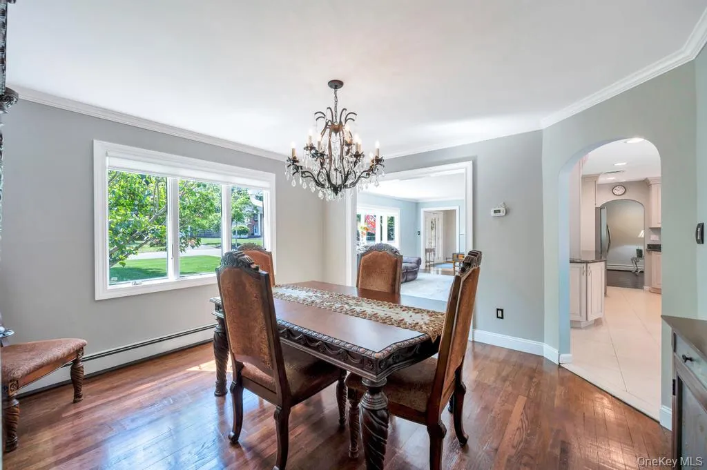 Formal dining space featuring wood-finish flooring, a contemporary chandelier, crown molding, and a wide window with white trim Formal dining space featuring wood-finish flooring, a contemporary chandelier, crown molding, and a wide window with white trim
