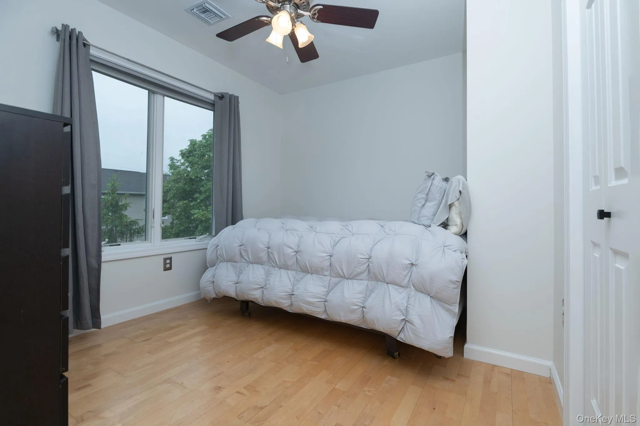 Room featuring light wood-finish flooring, a contemporary ceiling fan, and a double-pane window with a white frame Room featuring light wood-finish flooring, a contemporary ceiling fan, and a double-pane window with a white frame