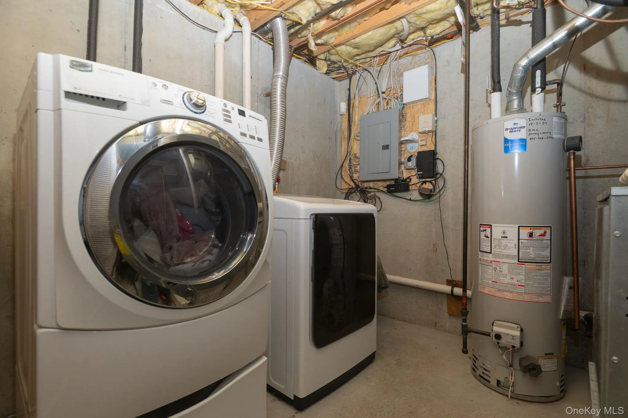 Laundry area featuring a front-loading washing machine, electric dryer, and water heater Laundry area featuring a front-loading washing machine, electric dryer, and water heater