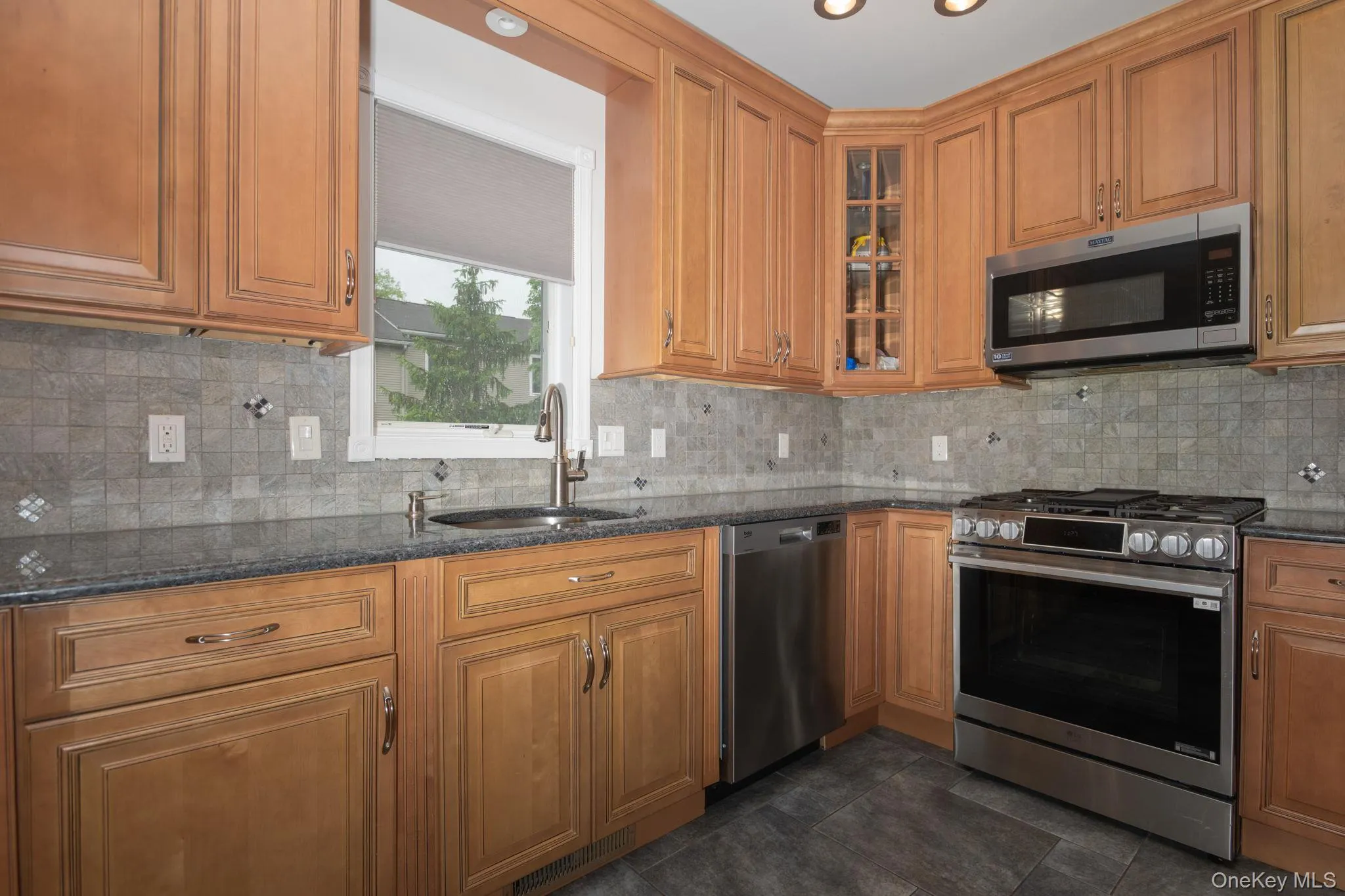Kitchen featuring wood cabinetry, stone countertops, a tile backsplash, stainless steel appliances, and tile flooring Kitchen featuring wood cabinetry, stone countertops, a tile backsplash, stainless steel appliances, and tile flooring