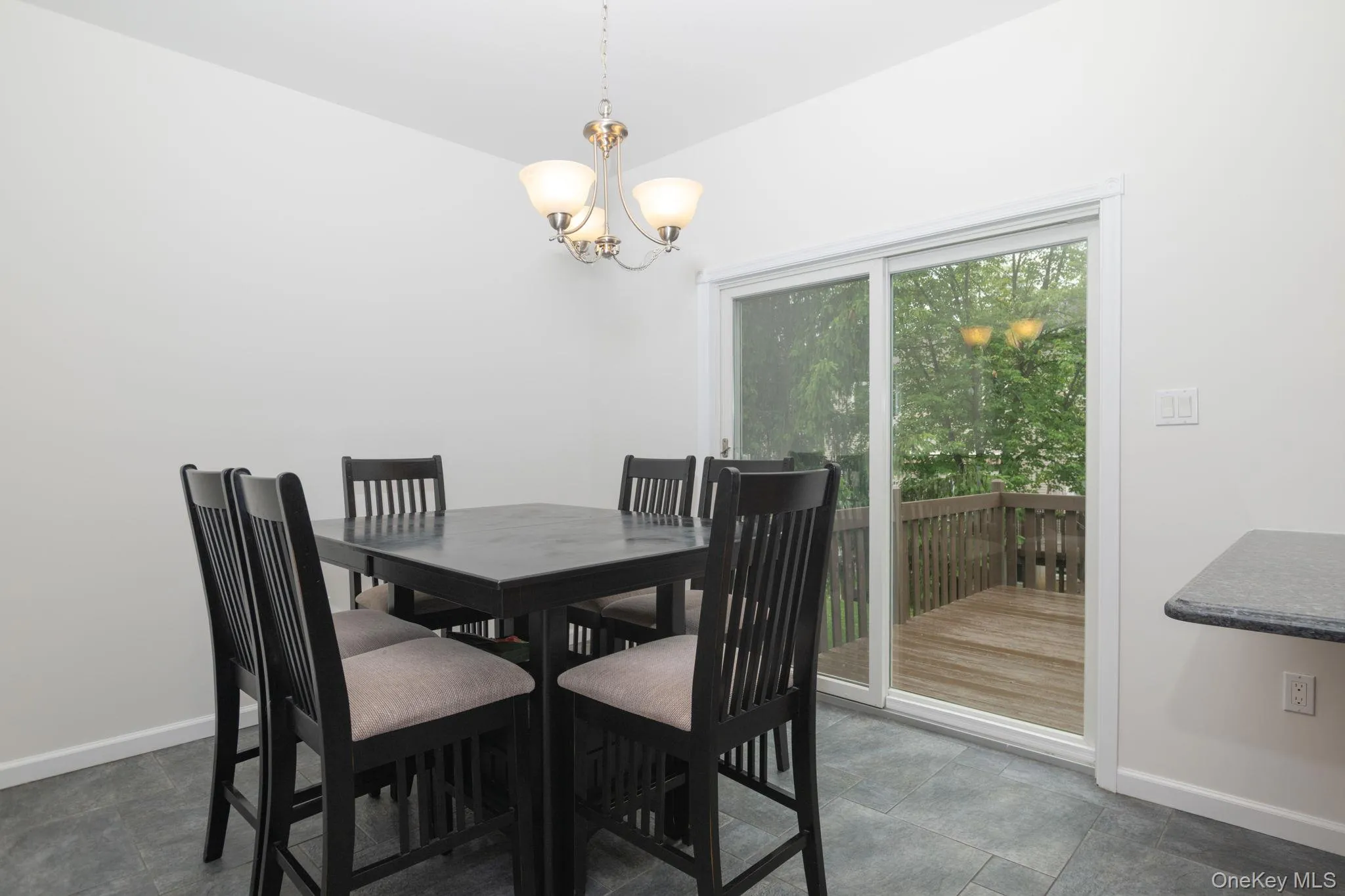 Dining area featuring tile flooring, a brushed nickel chandelier, white walls, and a sliding glass door providing access to an outdoor deck Dining area featuring tile flooring, a brushed nickel chandelier, white walls, and a sliding glass door providing access to an outdoor deck
