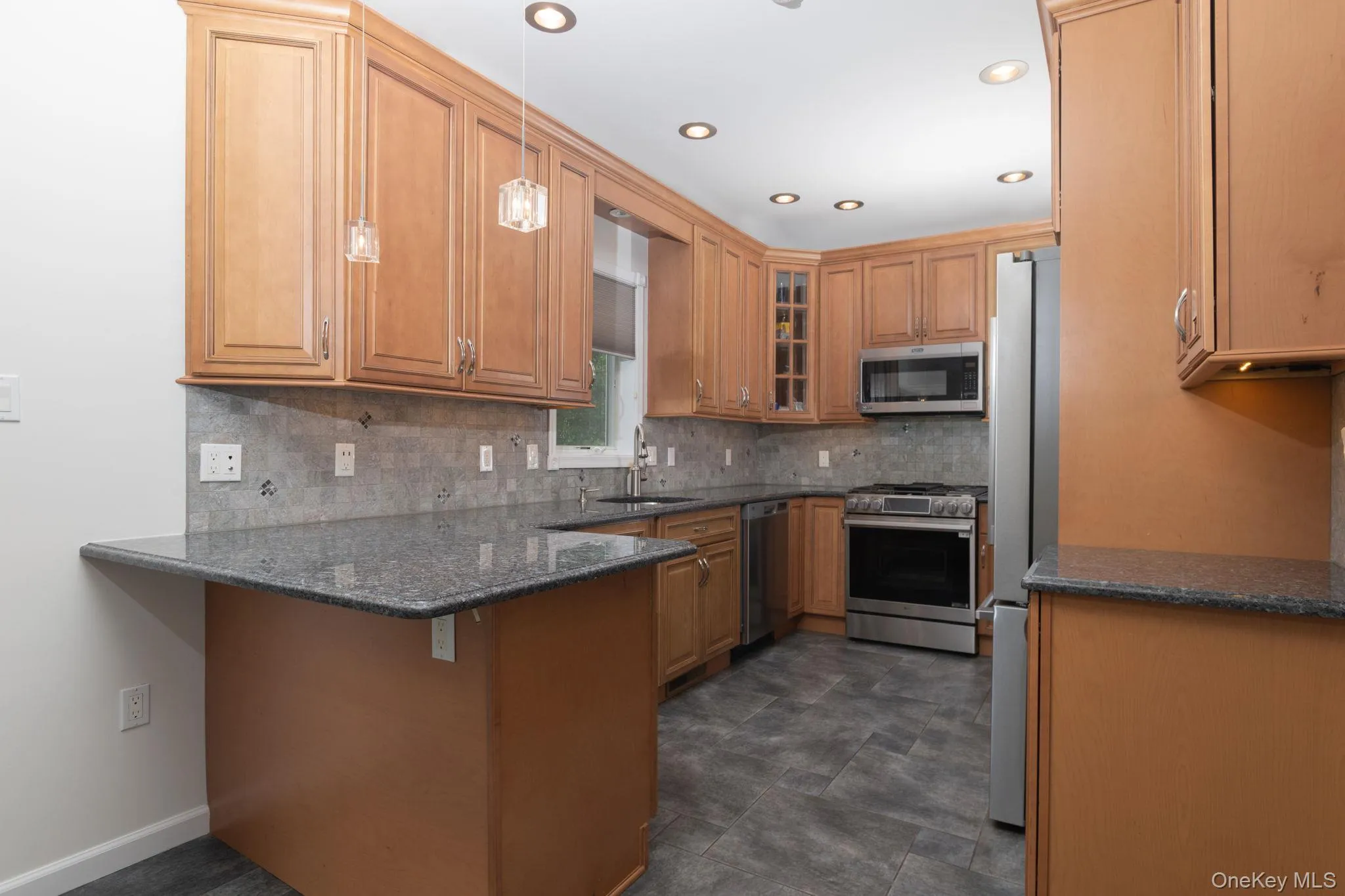 Kitchen featuring wood cabinetry, dark granite countertops, stainless steel appliances, recessed lighting, and tile flooring Kitchen featuring wood cabinetry, dark granite countertops, stainless steel appliances, recessed lighting, and tile flooring