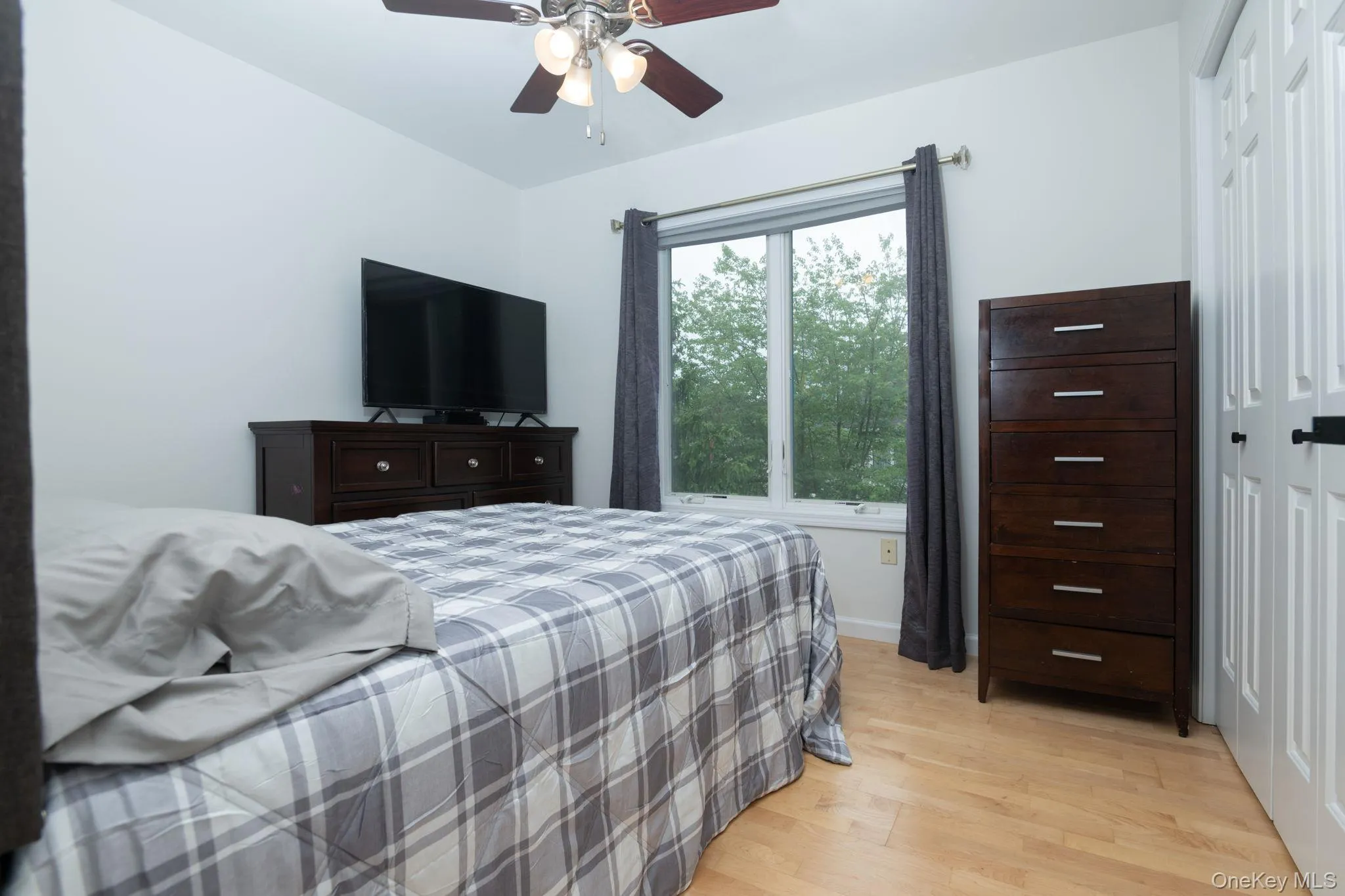 Bedroom featuring light wood-finish flooring, a ceiling fan with integrated lighting, and white paneled doors Bedroom featuring light wood-finish flooring, a ceiling fan with integrated lighting, and white paneled doors