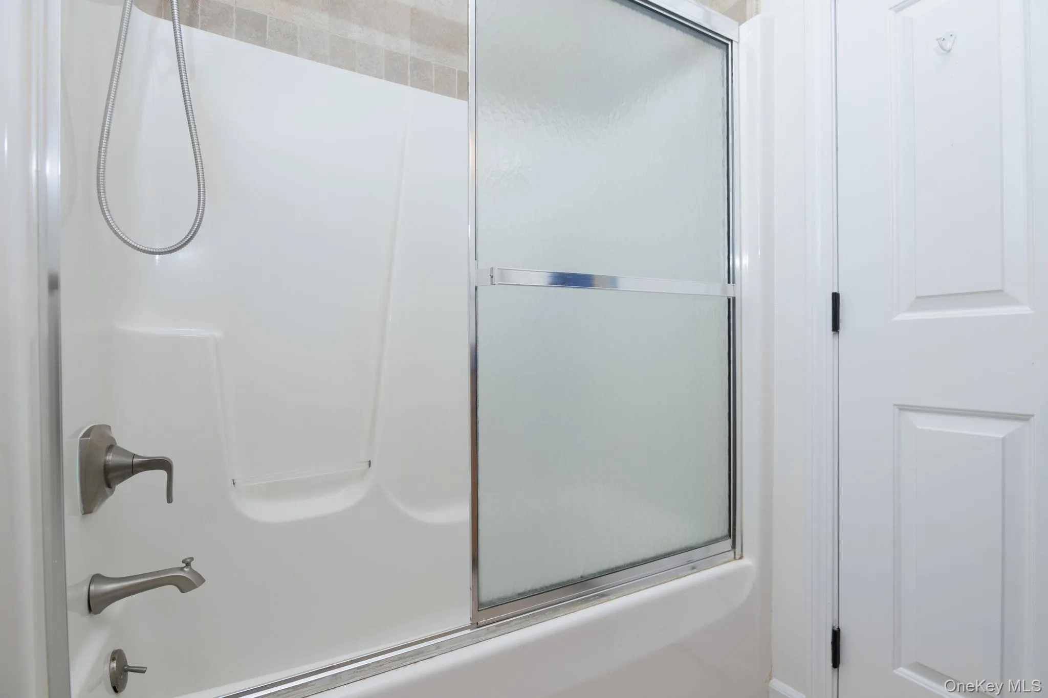 White tub and shower combination with brushed nickel fixtures and a tiled surround White tub and shower combination with brushed nickel fixtures and a tiled surround