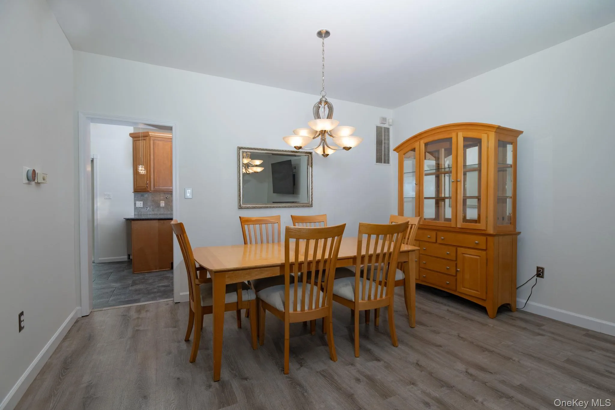 Spacious dining area featuring wood-finish flooring, neutral wall paint, and an overhead chandelier light fixture Spacious dining area featuring wood-finish flooring, neutral wall paint, and an overhead chandelier light fixture