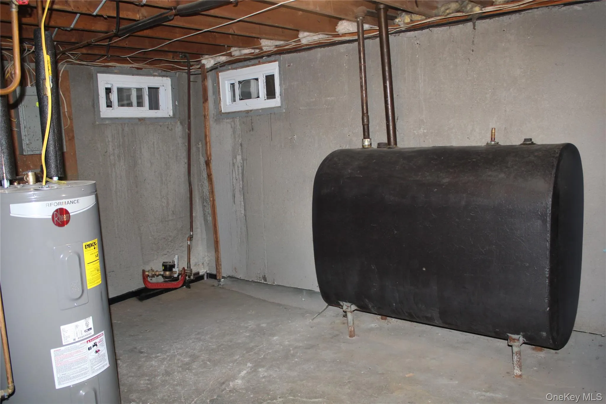 Utility area featuring a water heater, oil tank, exposed joists, and concrete walls and flooring Utility area featuring a water heater, oil tank, exposed joists, and concrete walls and flooring