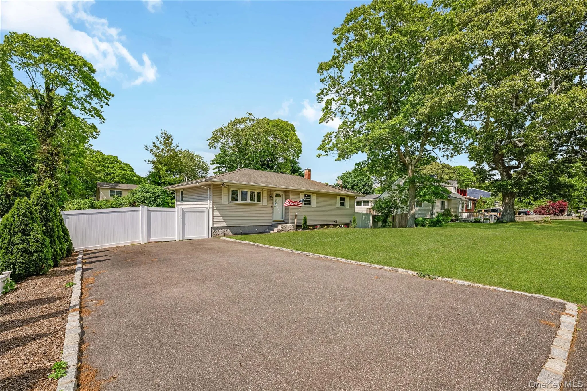 Ranch-style residence featuring light-colored siding, a paved driveway, and a white privacy fence Ranch-style residence featuring light-colored siding, a paved driveway, and a white privacy fence