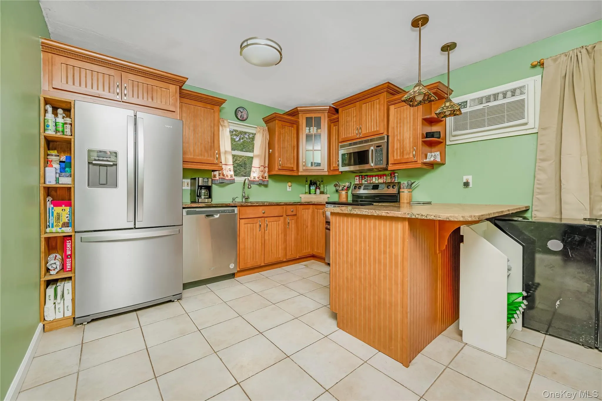Kitchen featuring wood cabinetry, stainless steel appliances, and a built-in island with a countertop extension Kitchen featuring wood cabinetry, stainless steel appliances, and a built-in island with a countertop extension