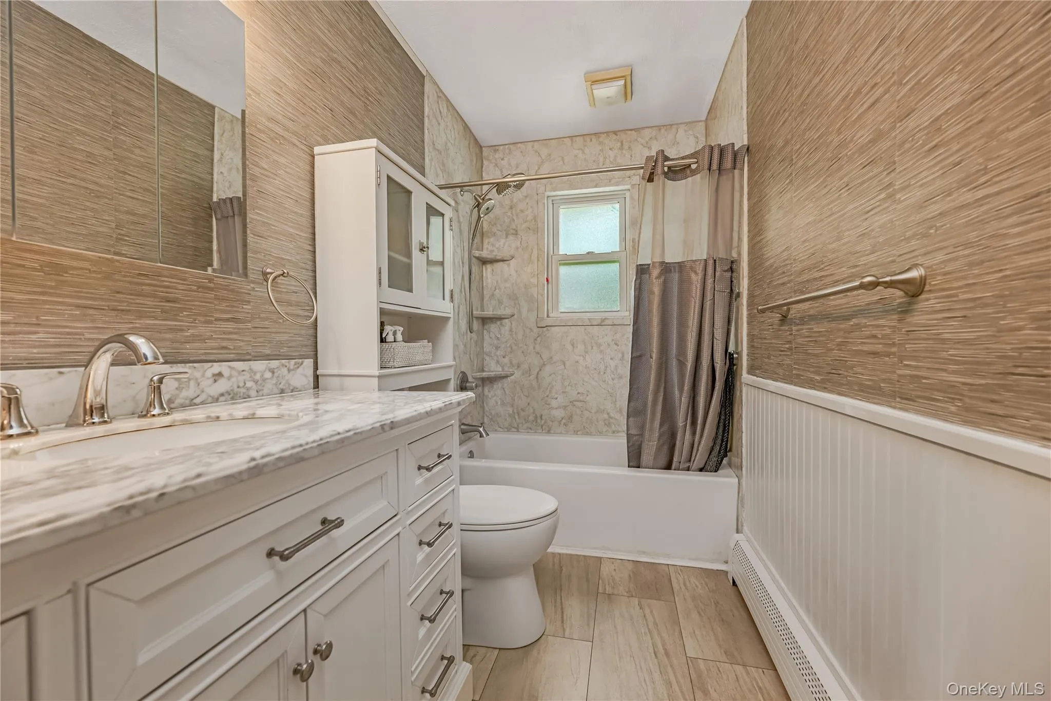 Bathroom featuring a white vanity with a marble-finish countertop, wood-finish flooring, a built-in tub with shower, and wainscoting Bathroom featuring a white vanity with a marble-finish countertop, wood-finish flooring, a built-in tub with shower, and wainscoting