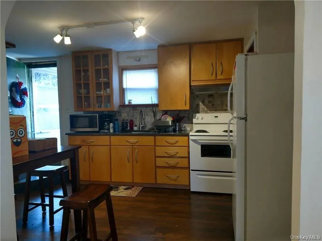 Kitchen with a sink, dark wood finished floors, decorative backsplash, glass insert cabinets, and white appliances Kitchen with a sink, dark wood finished floors, decorative backsplash, glass insert cabinets, and white appliances
