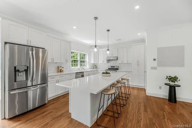 Kitchen featuring white shaker cabinetry, stainless steel appliances, a center island with countertop seating, recessed lighting, and wood-finish flooring Kitchen featuring white shaker cabinetry, stainless steel appliances, a center island with countertop seating, recessed lighting, and wood-finish flooring