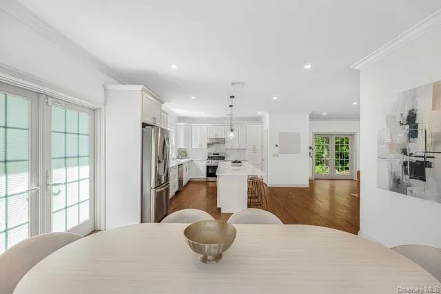Open-concept living area featuring hardwood flooring, recessed lighting, crown molding, and white French doors Open-concept living area featuring hardwood flooring, recessed lighting, crown molding, and white French doors