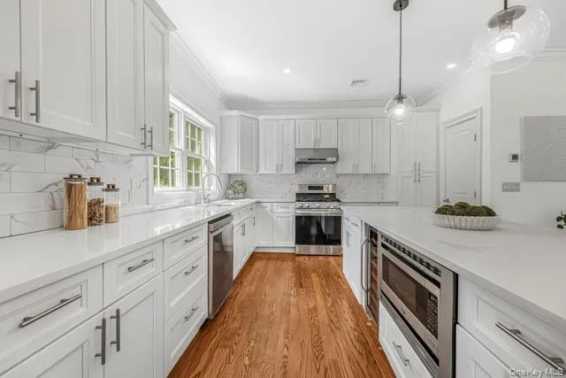 Spacious kitchen featuring white shaker cabinetry, quartz countertops, a subway tile backsplash, stainless steel appliances, and wood-finish flooring Spacious kitchen featuring white shaker cabinetry, quartz countertops, a subway tile backsplash, stainless steel appliances, and wood-finish flooring