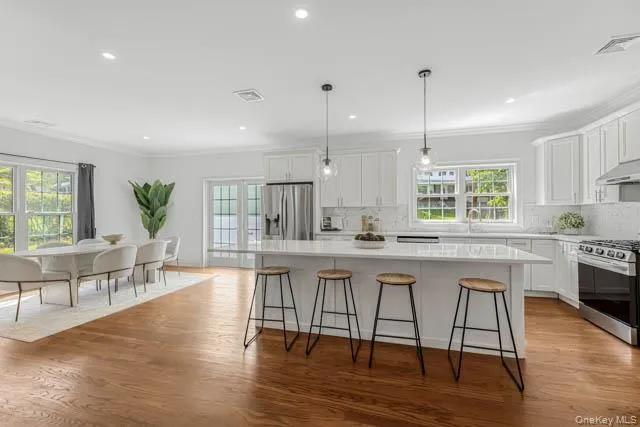 Spacious kitchen featuring white shaker cabinetry, stainless steel appliances, a large center island with seating, and wood-finish flooring Spacious kitchen featuring white shaker cabinetry, stainless steel appliances, a large center island with seating, and wood-finish flooring