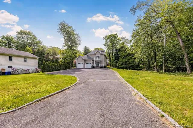 Paved driveway approaching a light-colored exterior with a front porch and two garage doors Paved driveway approaching a light-colored exterior with a front porch and two garage doors