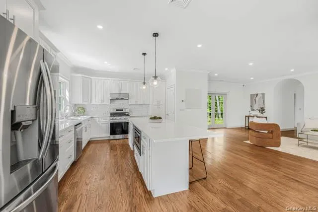 Expansive kitchen featuring white cabinetry, stainless steel appliances, a center island with pendant lighting, and wood-finish flooring Expansive kitchen featuring white cabinetry, stainless steel appliances, a center island with pendant lighting, and wood-finish flooring