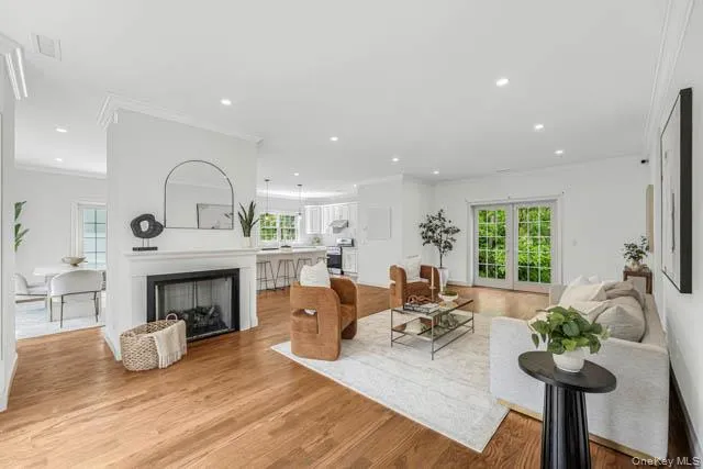 Hardwood flooring extends throughout this open-concept living space, featuring a fireplace with a white mantel and a dark firebox Hardwood flooring extends throughout this open-concept living space, featuring a fireplace with a white mantel and a dark firebox