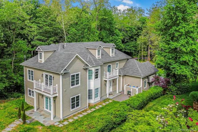 Expansive residence featuring multiple dormer windows, a balcony with white railings, and a lower-level patio with stone pavers Expansive residence featuring multiple dormer windows, a balcony with white railings, and a lower-level patio with stone pavers