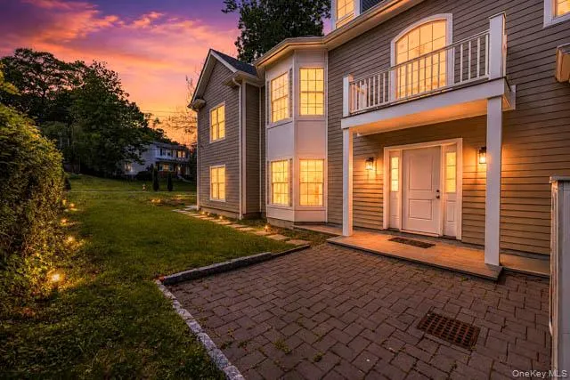 Exterior featuring a paver driveway, white front door with sidelights, upper balcony with white railings, a bay window, and exterior lighting Exterior featuring a paver driveway, white front door with sidelights, upper balcony with white railings, a bay window, and exterior lighting