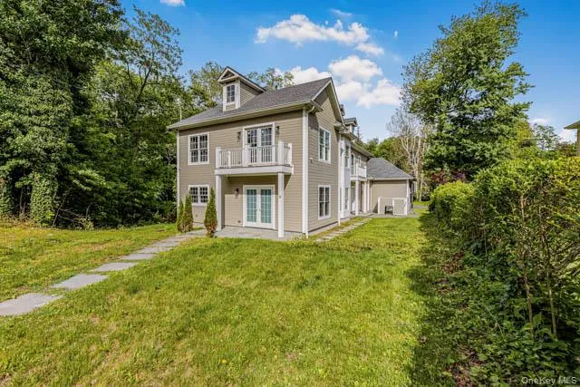 Contemporary two-story exterior with dormer window, featuring a second-story balcony with white railings, ground-level patio, and a stone walkway Contemporary two-story exterior with dormer window, featuring a second-story balcony with white railings, ground-level patio, and a stone walkway