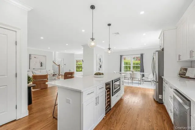 Expansive kitchen featuring a large central island with integrated wine cooler and microwave, white cabinetry, stainless steel appliances, and recessed lighting Expansive kitchen featuring a large central island with integrated wine cooler and microwave, white cabinetry, stainless steel appliances, and recessed lighting