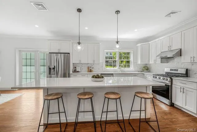 Modern kitchen featuring a large center island with seating, stainless steel appliances, white cabinetry, and wood-finish flooring Modern kitchen featuring a large center island with seating, stainless steel appliances, white cabinetry, and wood-finish flooring