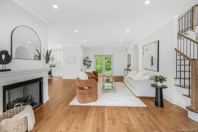 Spacious living area featuring hardwood flooring, a fireplace with a white mantel, recessed lighting, and a prominent staircase with dark metal balusters and a wood handrail Spacious living area featuring hardwood flooring, a fireplace with a white mantel, recessed lighting, and a prominent staircase with dark metal balusters and a wood handrail