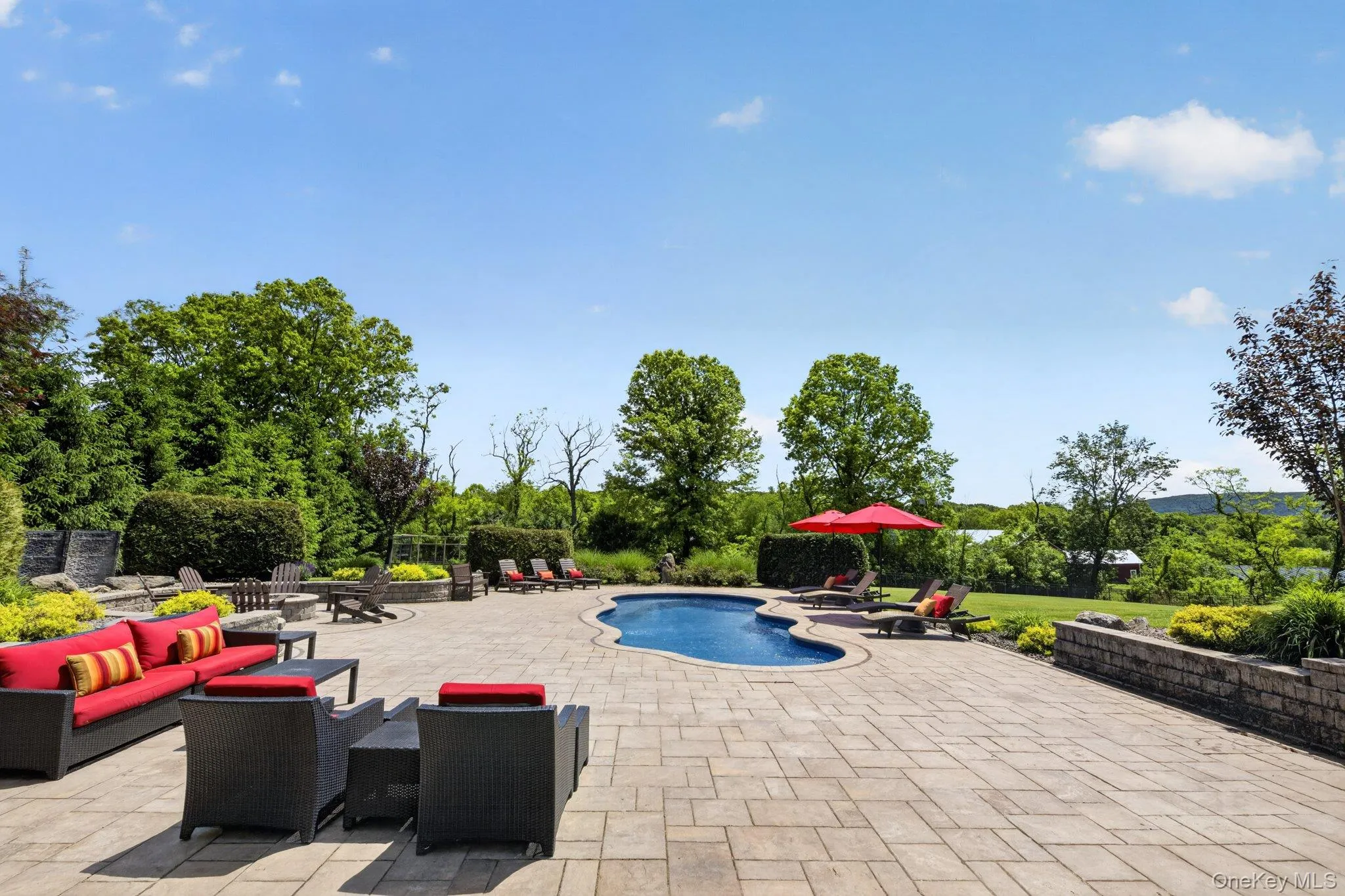 Expansive paver patio surrounding a freeform inground pool with stone-faced retaining walls and mature landscaping Expansive paver patio surrounding a freeform inground pool with stone-faced retaining walls and mature landscaping