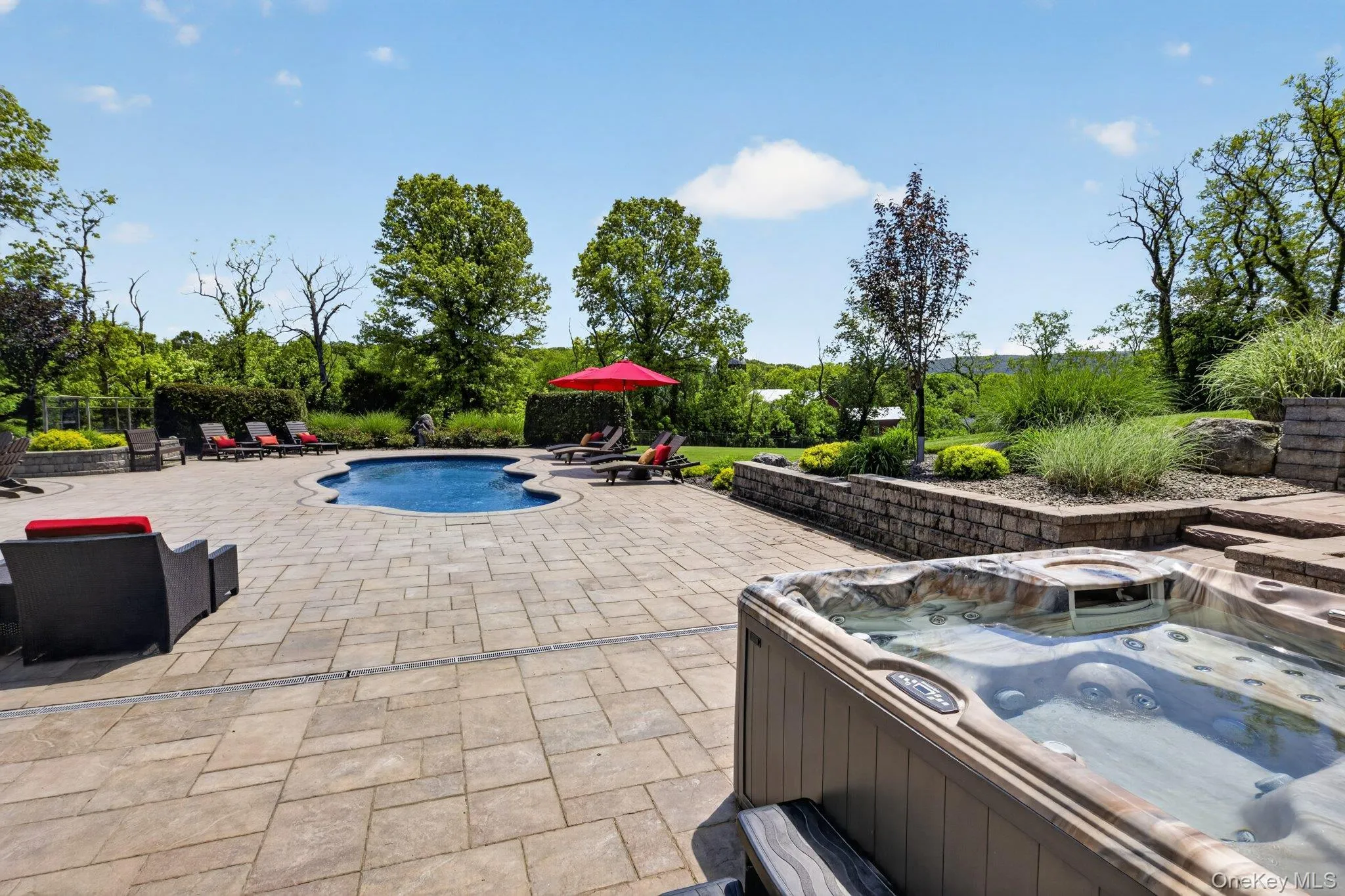 Expansive paver patio surrounding a freeform swimming pool and an integrated hot tub Expansive paver patio surrounding a freeform swimming pool and an integrated hot tub