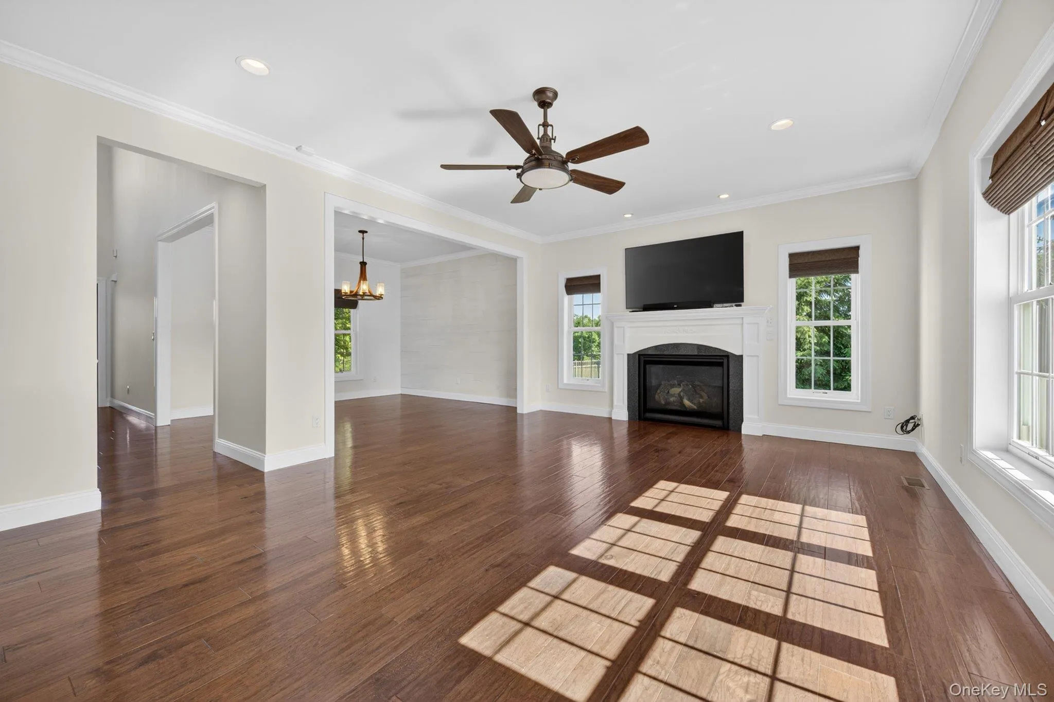 Spacious living area featuring wood-finish flooring, a fireplace with a white mantel, recessed lighting, and a ceiling fan Spacious living area featuring wood-finish flooring, a fireplace with a white mantel, recessed lighting, and a ceiling fan