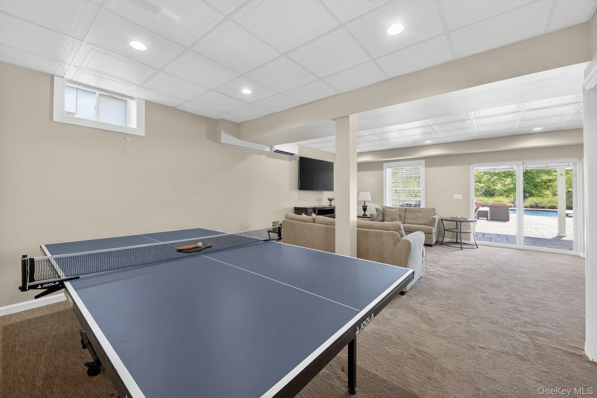 Finished lower level featuring recessed lighting, plush carpet flooring, a window providing natural light, and glass sliding doors opening to an outdoor patio with a pool Finished lower level featuring recessed lighting, plush carpet flooring, a window providing natural light, and glass sliding doors opening to an outdoor patio with a pool