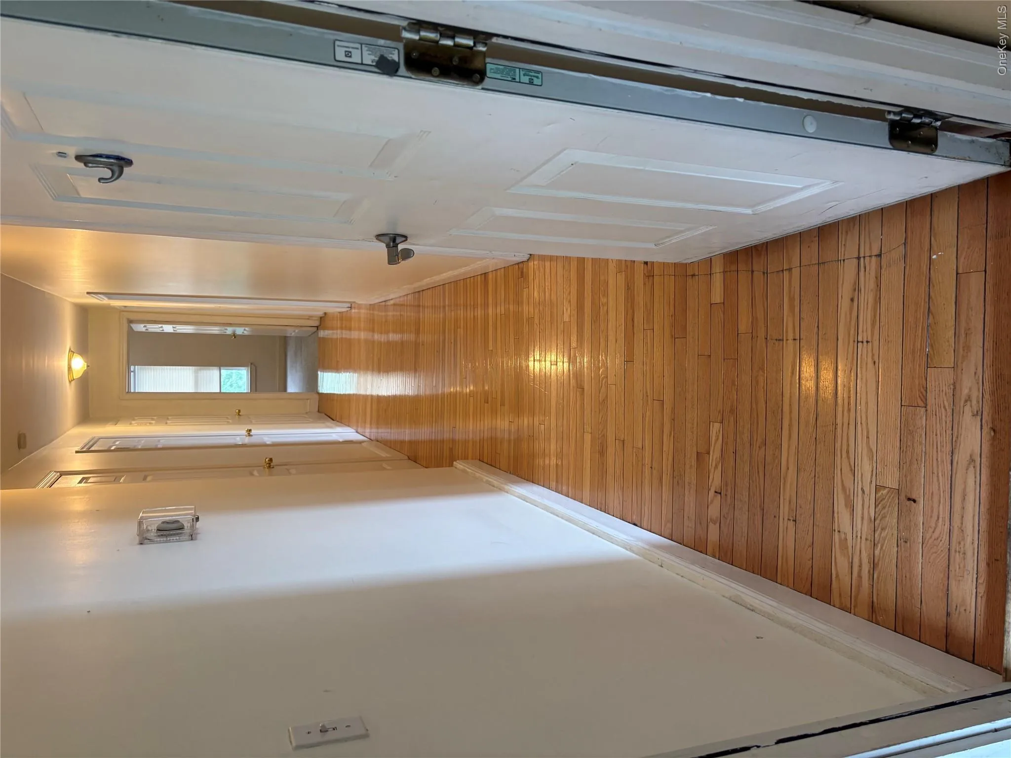 Hallway featuring wood-finish flooring, white painted walls, and a ceiling-mounted light fixture Hallway featuring wood-finish flooring, white painted walls, and a ceiling-mounted light fixture