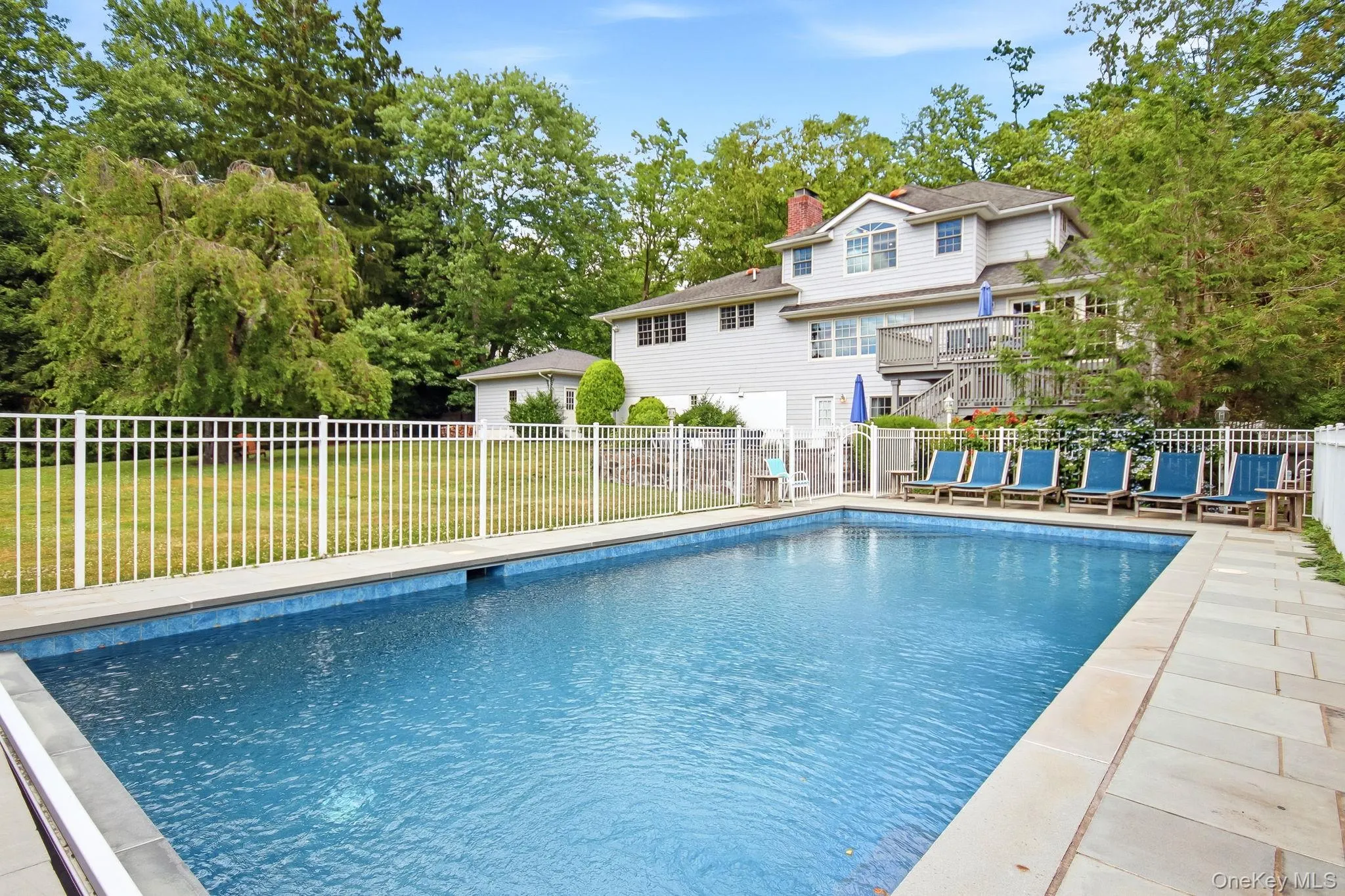 In-ground swimming pool with surround, featuring a white fence In-ground swimming pool with surround, featuring a white fence