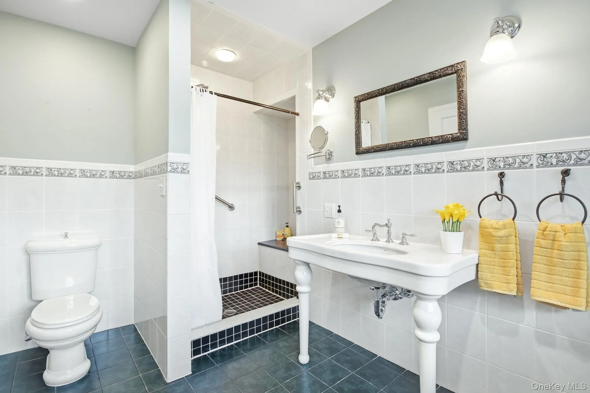Primary en-suite bathroom featuring a walk-in shower with a built-in seat, white subway tile walls with decorative border, and a classic pedestal sink Primary en-suite bathroom featuring a walk-in shower with a built-in seat, white subway tile walls with decorative border, and a classic pedestal sink