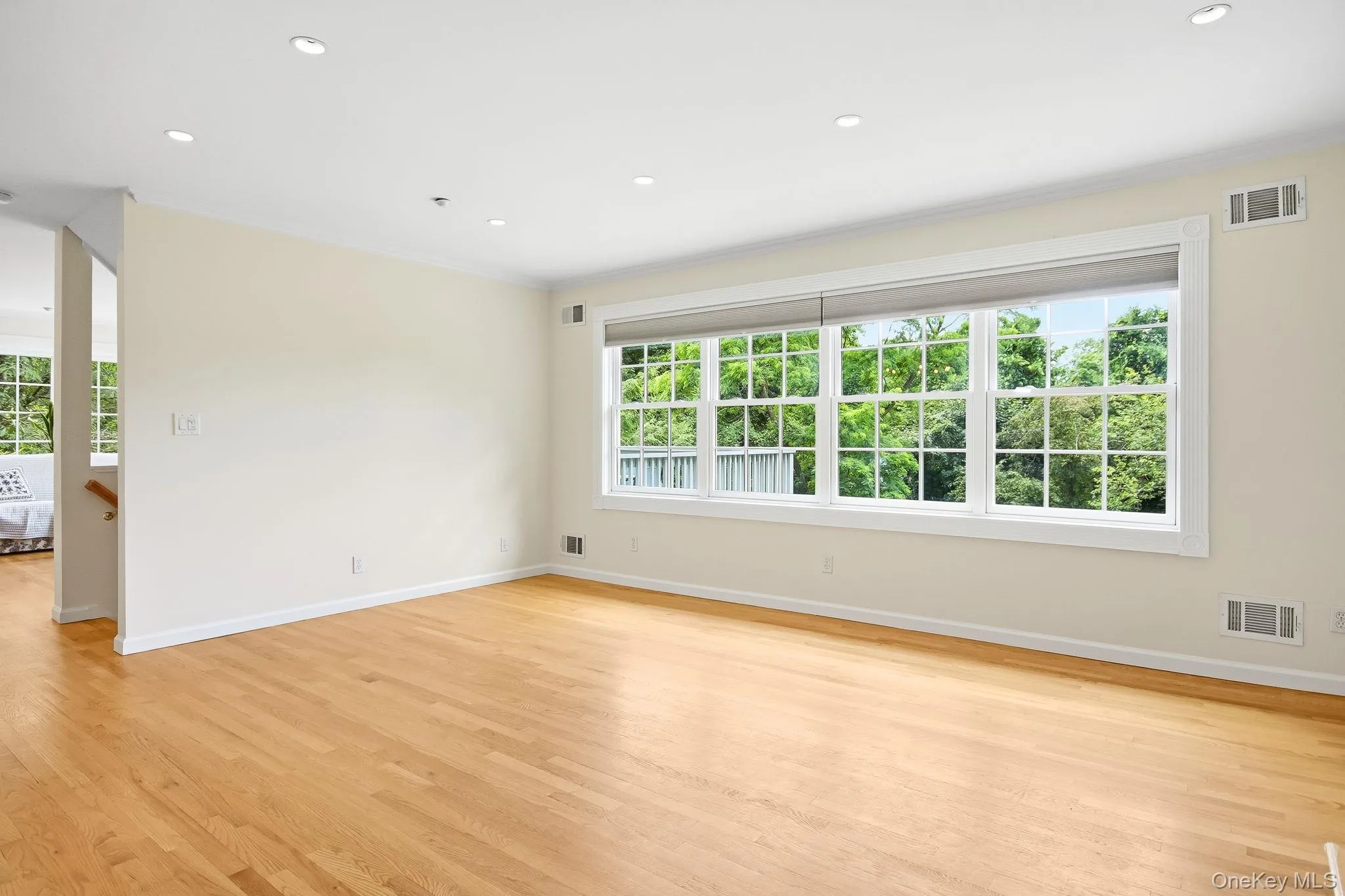 Expansive living room featuring hardwood flooring, recessed ceiling lighting, and a large multi-pane window Expansive living room featuring hardwood flooring, recessed ceiling lighting, and a large multi-pane window