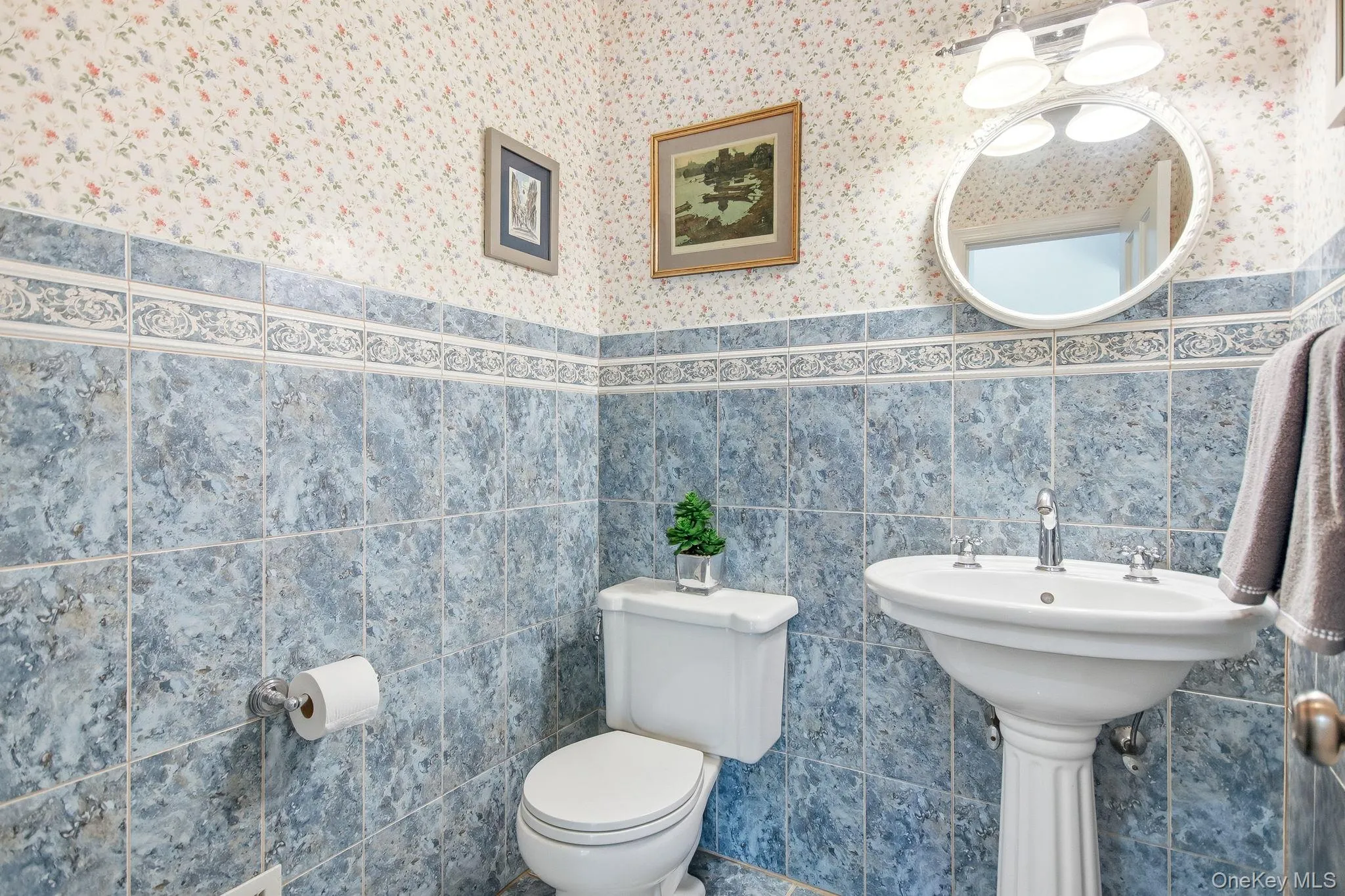 Powder room featuring a pedestal sink with chrome faucet, complemented by blue patterned wall tiling and a decorative border Powder room featuring a pedestal sink with chrome faucet, complemented by blue patterned wall tiling and a decorative border