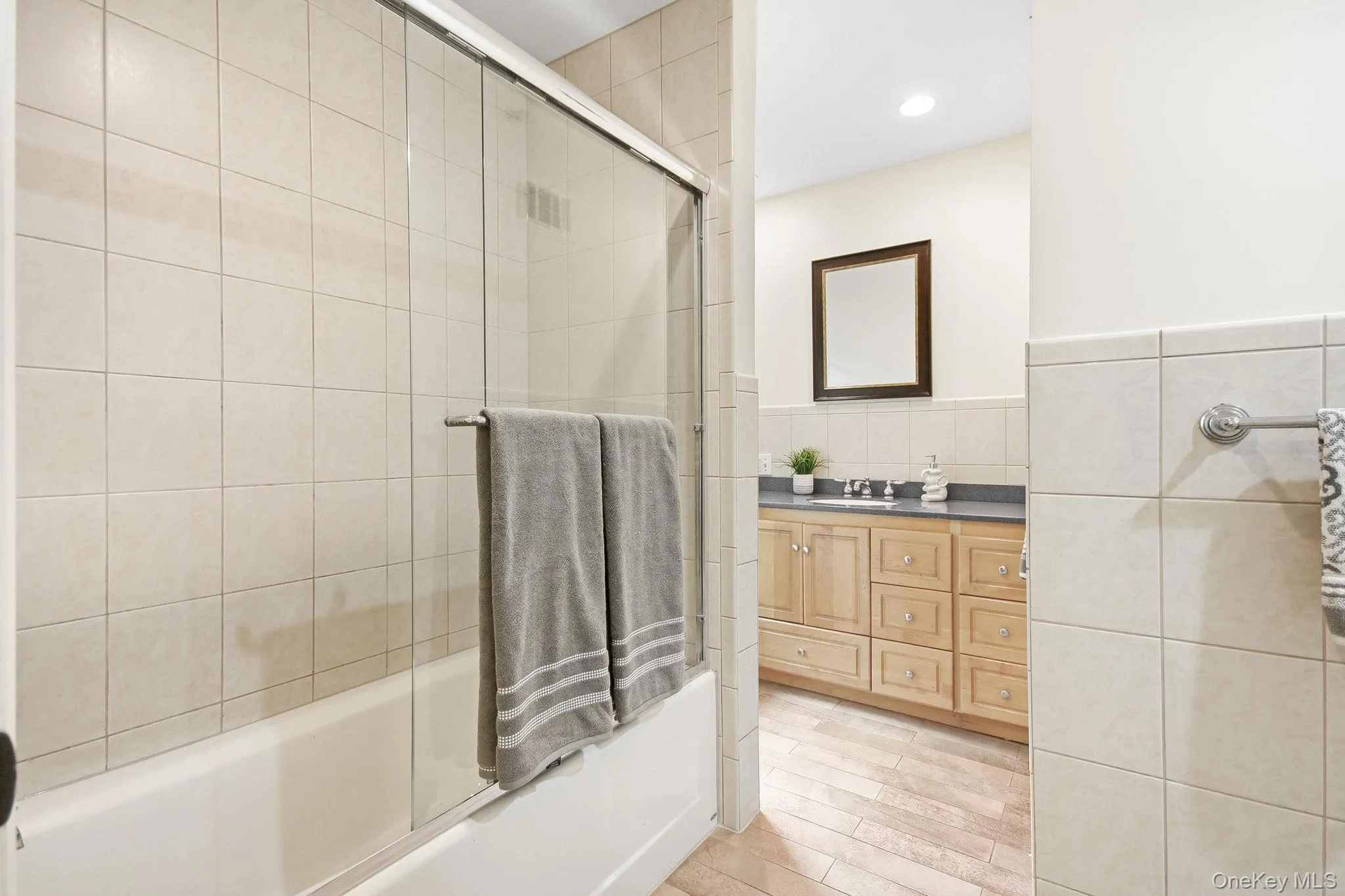 Second en-suite full bathroom; tiled bathtub with glass sliding doors, vanity and window Second en-suite full bathroom; tiled bathtub with glass sliding doors, vanity and window